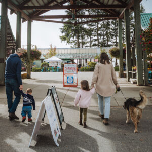 A family with children and a dog walking into Spirit Square Farmers’ Market at Harbour Quay in Port Alberni.