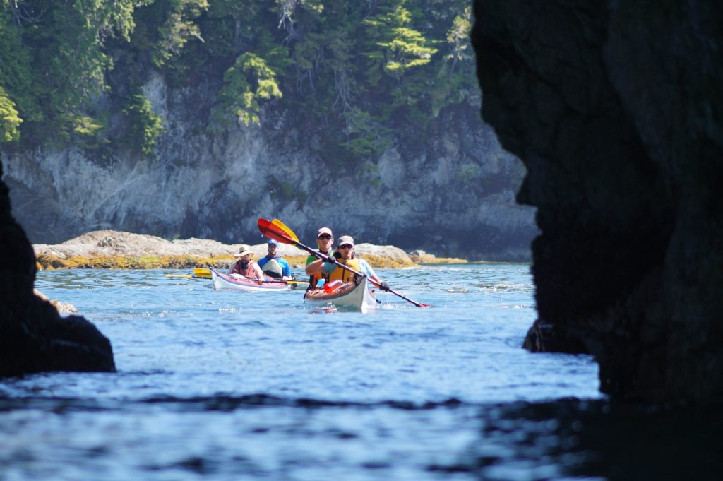 Sea kayakers paddling along the coastline during a multi-day expedition with Batstar Sea Kayak Outfitters