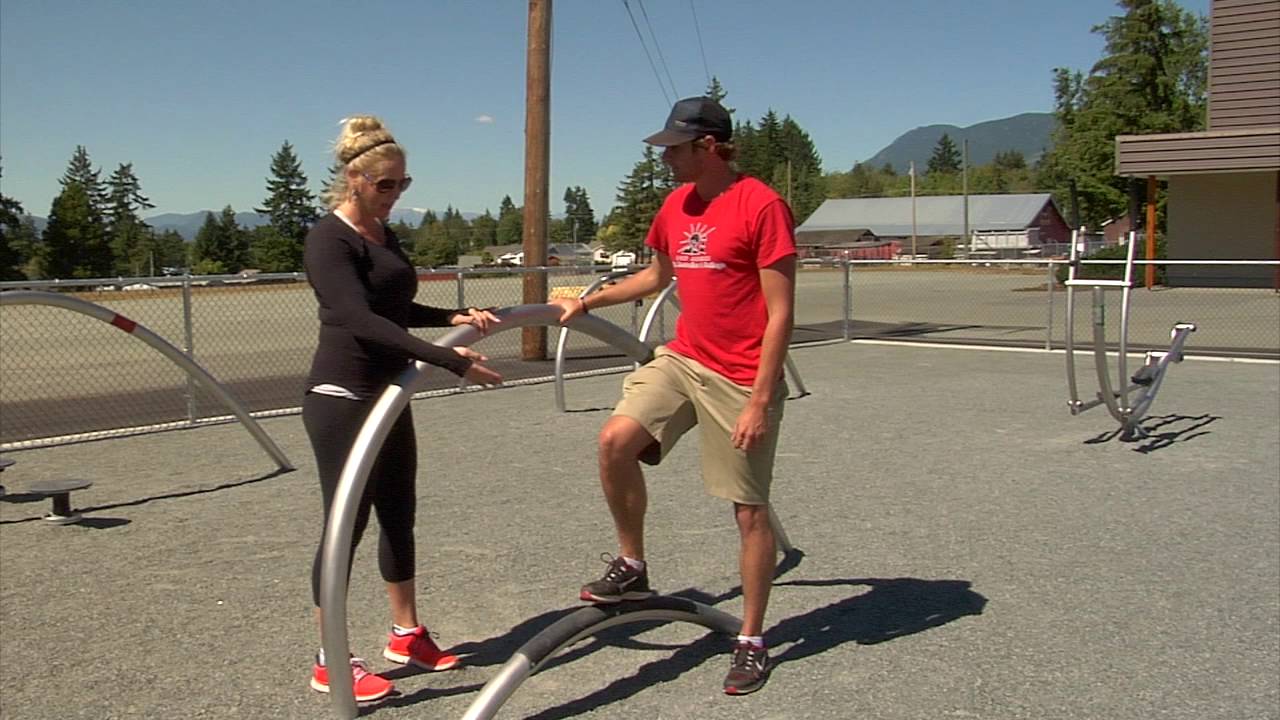 Woman showing man how to use exercise equipment at Bob Dailey Outdoor Fitness Park, Alberni Valley