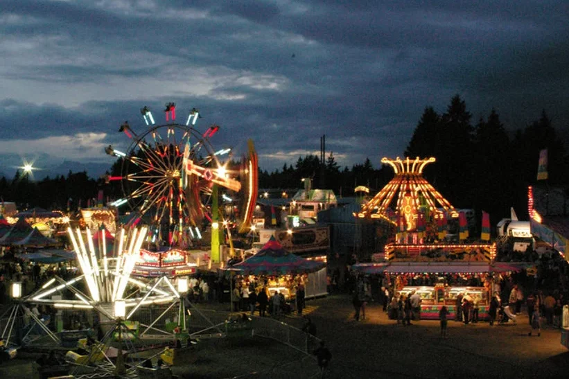 A nighttime scene of a brightly lit carnival with rides and crowds during the Fall Fair.