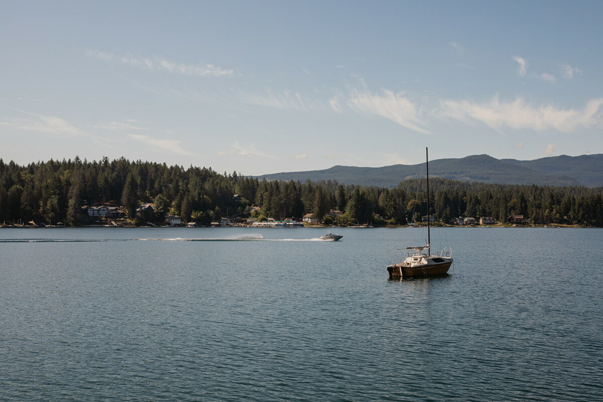 Boat and waterskier on Sproat Lake with forested shoreline and mountains in the background