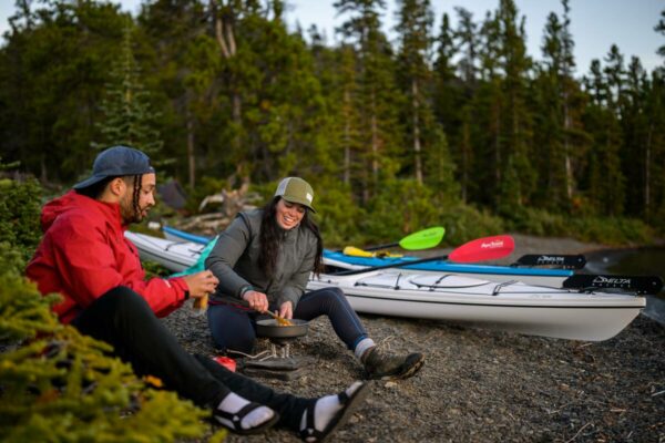 Two kayakers prepare dinner on the beach of Sloko Island, in Atlin/Áa Tlein Téi x 'i Provincial Park. Atlin Lake is located in the remote northwest corner of British Columbia - the traditional territory of the Taku River Tlingit First Nation.