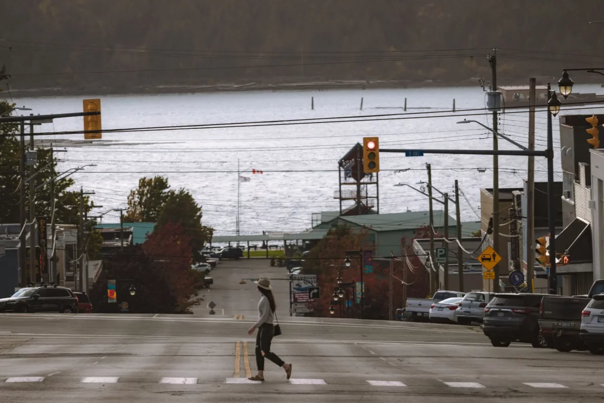 Solo traveller crossing a downtown Port Alberni street with the Alberni Inlet in the background