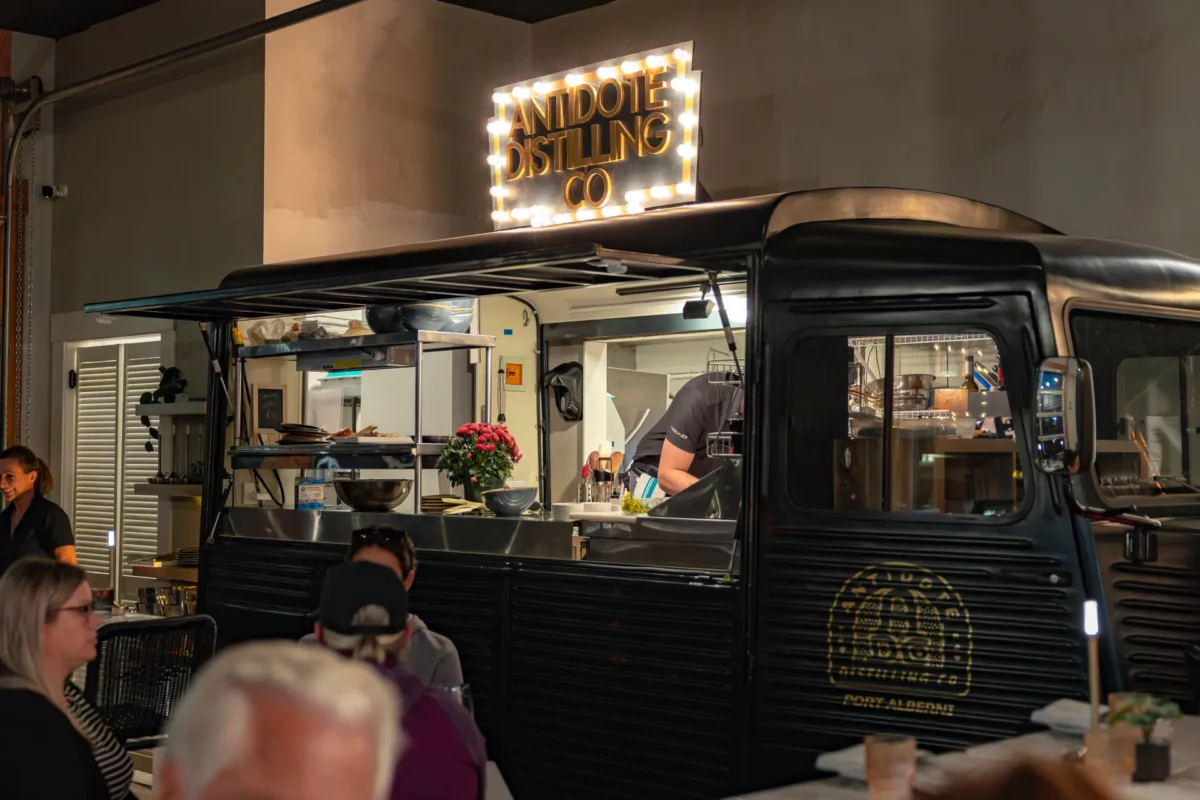 A vintage-style food truck serving drinks inside Antidote Distilling Co., with a glowing sign above.