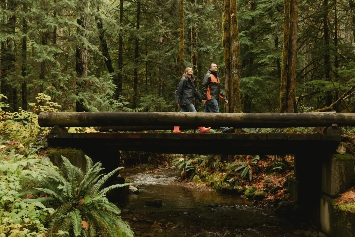 A couple walking across a wooden bridge on Rogers Creek Trail, surrounded by lush green forest.