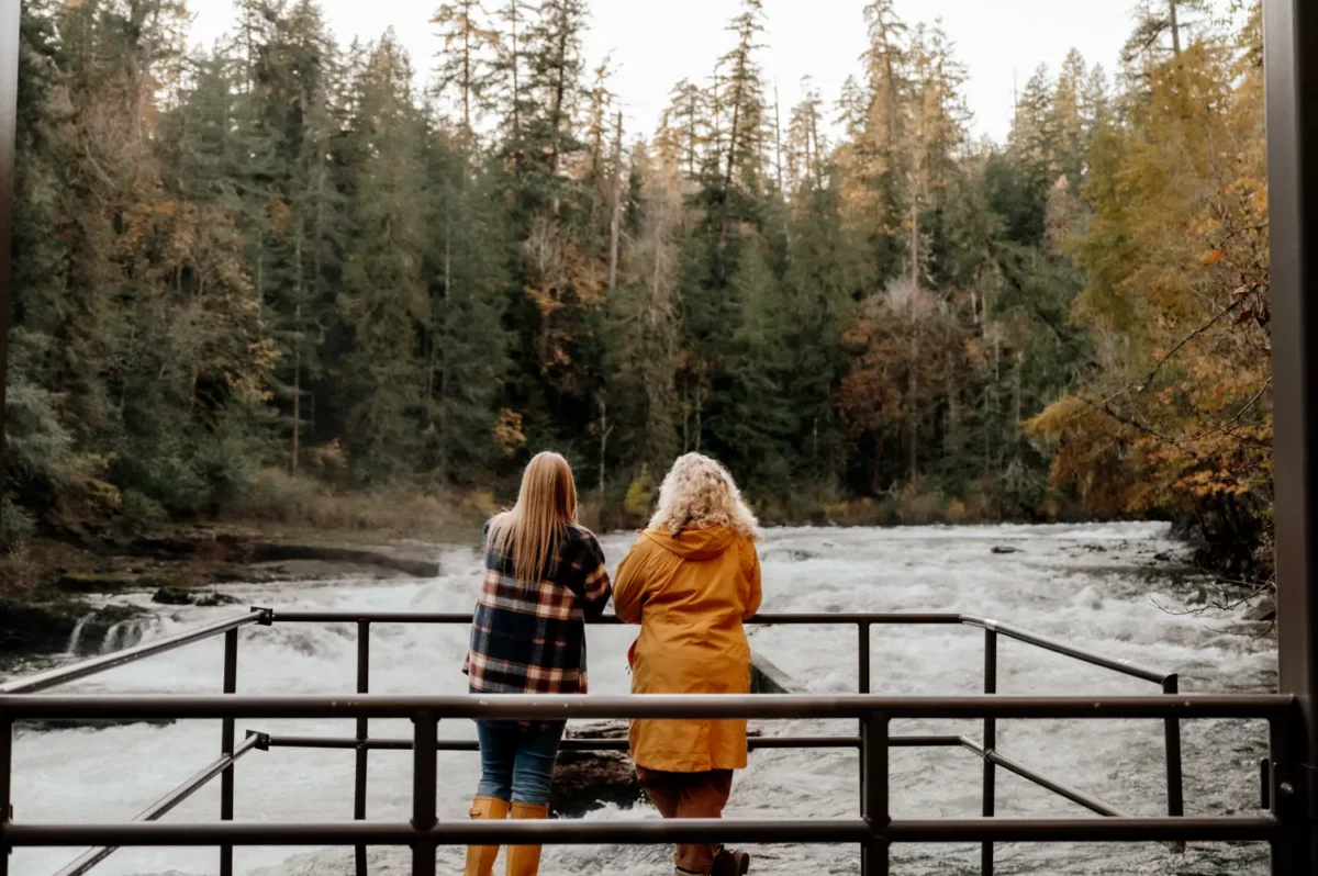 Two people standing at a viewing platform overlooking the rushing water and forest at Stamp Falls in Port Alberni on a rainy winter day.