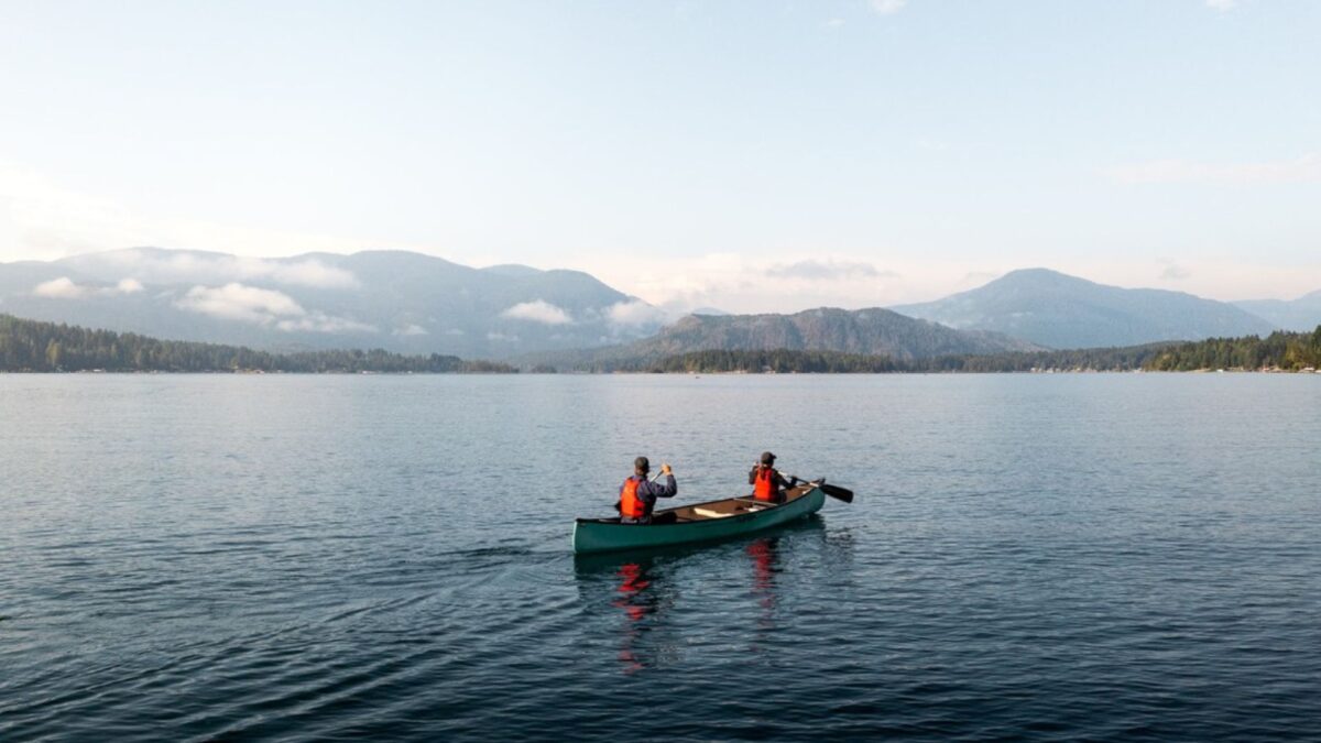 Two people paddling a canoe on Sproat Lake with mountain views in the background