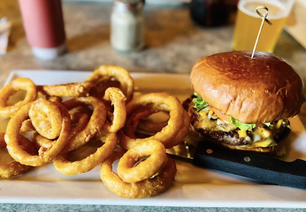 Mushroom cheeseburger topped with lettuce and melted cheese on a toasted bun, served with crispy golden onion rings at Bucksnort’s Bar & Grill in Port Alberni.
