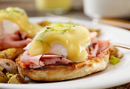 Close-up of an eggs benedict served on a toasted English muffin with shaved ham, poached egg, and creamy hollandaise, plated with breakfast potatoes at Pescadores Bistro in Port Alberni.
