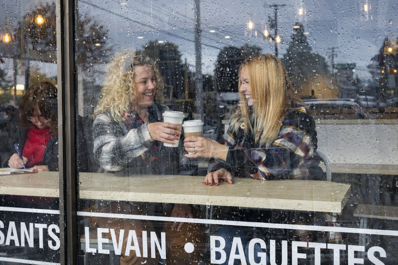 Friends enjoying coffee inside a café while rain falls on the window along Argyle Street in Port Alberni