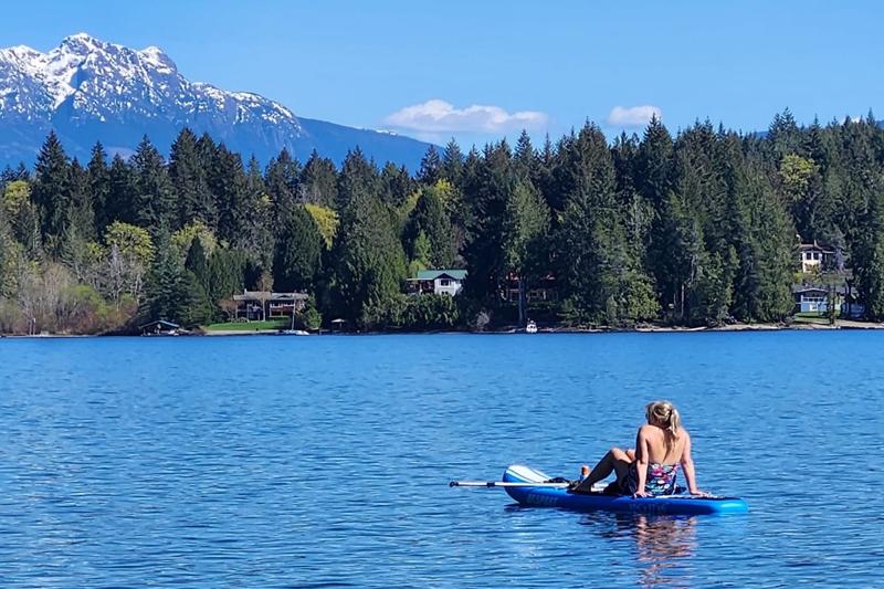 Paddleboarder relaxing on Sproat Lake with forest and mountain backdrop