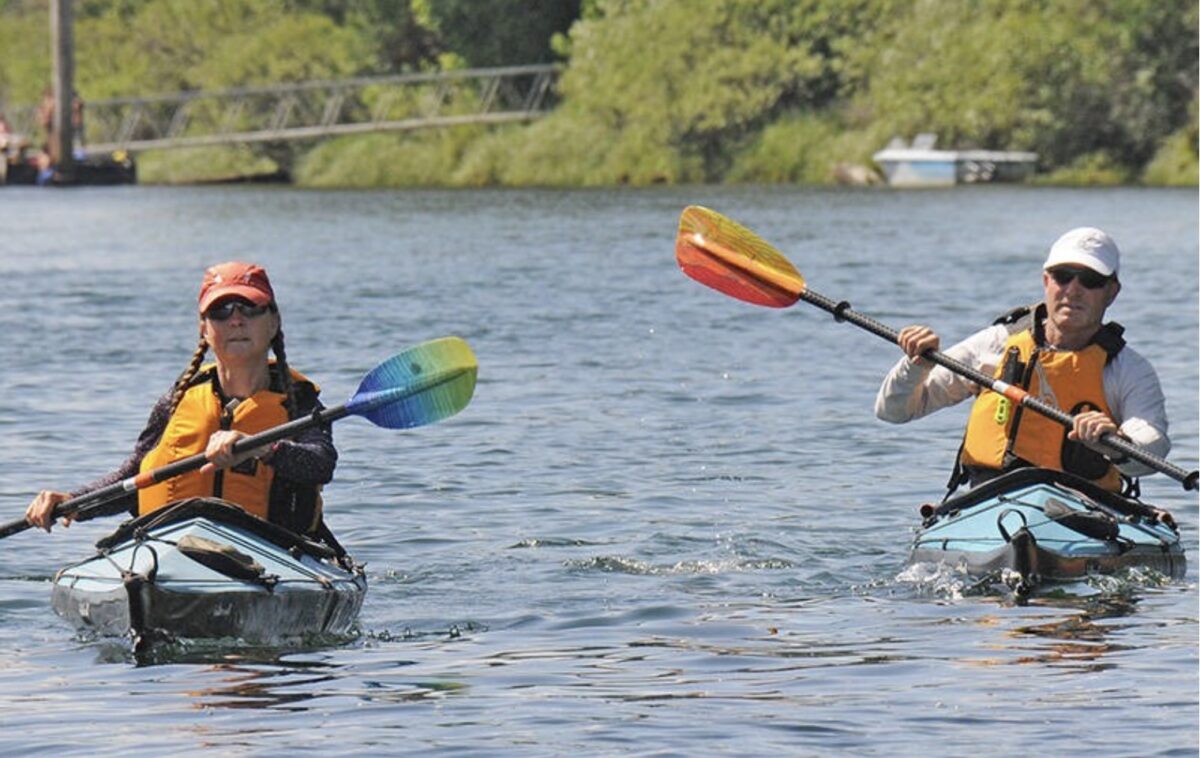 Two people kayaking on calm water in the Alberni Valley during summer.